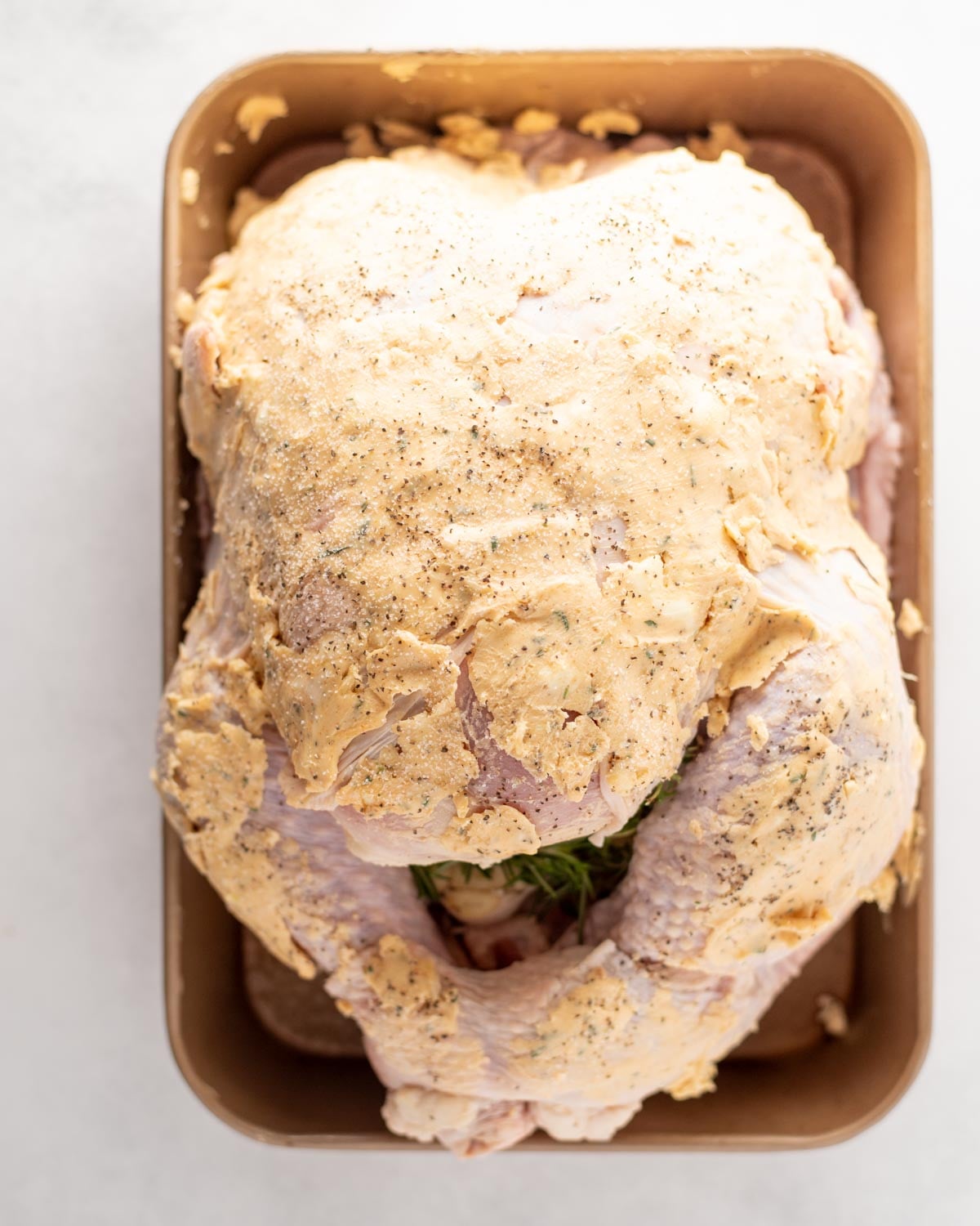 A raw whole turkey covered in seasoned herb butter, resting in a roasting pan.
