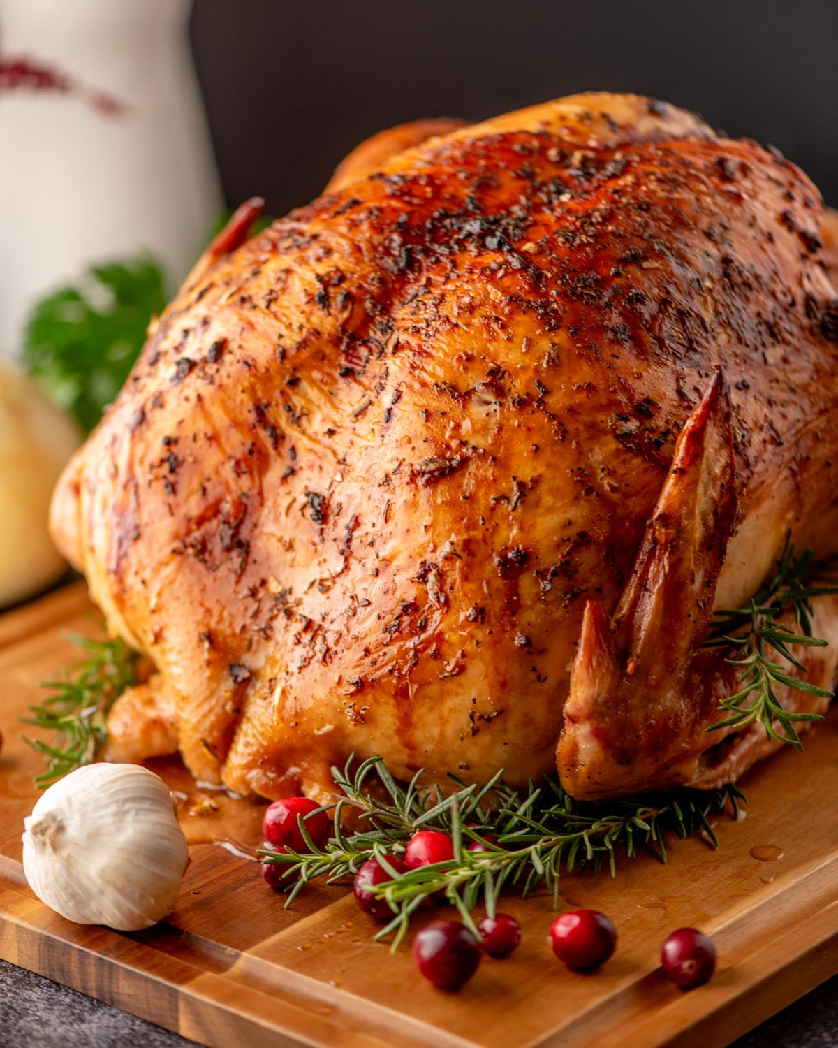 A roasted whole chicken on a wooden cutting board, garnished with fresh rosemary, garlic, and cranberries.
