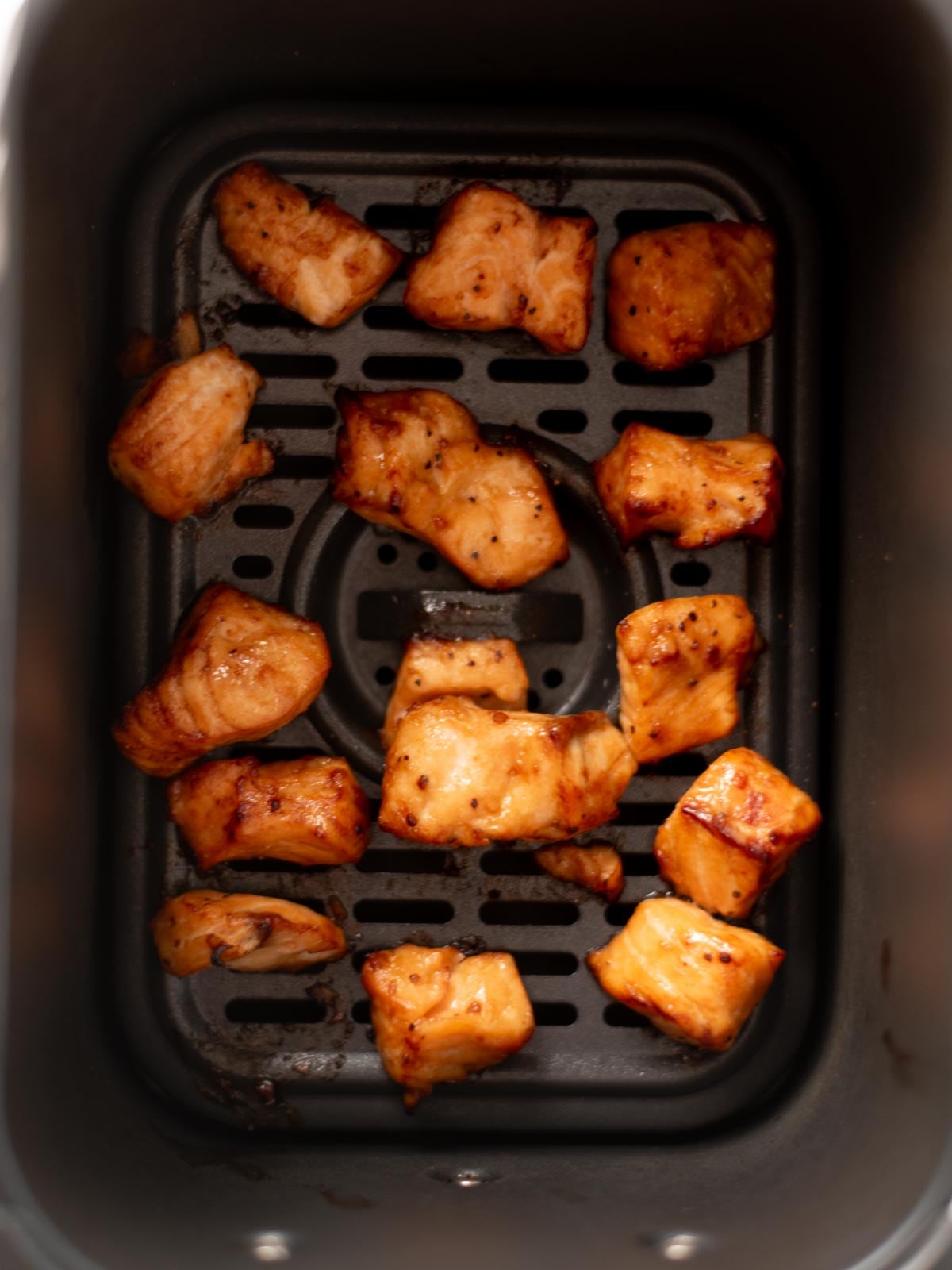 Bite-sized pieces of cooked, seasoned chicken in an air fryer basket.